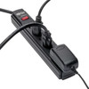 An angled close-up view of the black Tripp Lite surge protector against a white background, demonstrating various items plugged in. Two standard black power cords and one large, bulky AC adapter block are plugged into the outlets, highlighting how the end outlet accommodates oversized transformers.