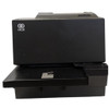 A low-angle, straight-on front shot emphasizing the check-feeding tray extension at the bottom. The main body of the dark gray printer rises up behind the tray, featuring the white circular NCR logo prominently printed on the front-left panel.