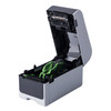 Side three-quarter view of the Brother TD-2310D desktop label printer with its top cover open, exposing the internal media roll compartment and green loading guides.