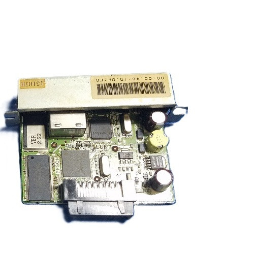An angled, top-down view of a green printed circuit board (PCB) for an Epson interface card. The top edge features a silver metal mounting bracket with a barcode and a MAC address sticker. The board itself is populated with various electronic components, including surface-mount chips, silver oscillators, and colorful capacitors. A black multi-pin connector is prominent at the bottom center of the board.