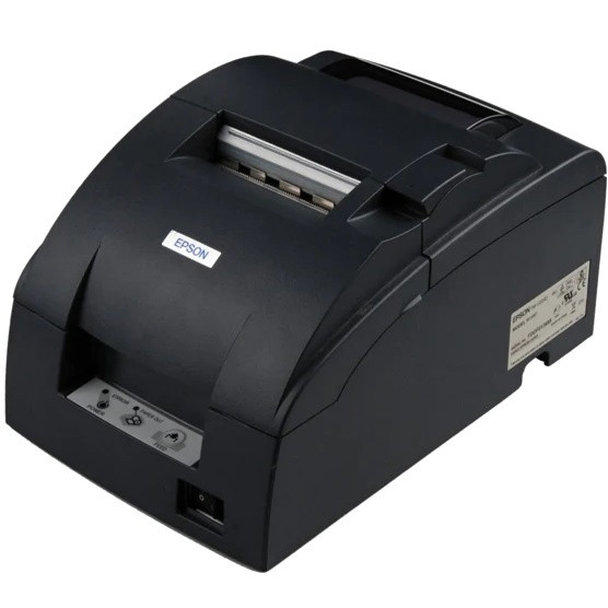 A three-quarter isometric view from the rear and side of the dark gray Epson impact kitchen printer. This perspective highlights the curved top and side form. The paper well is open, revealing the internal silver metal mechanism and rollers. The primary side panel clearly displays the detailed white product label containing serial numbers, regulatory marks, and configuration data, while the interface ports are visible at the rear-bottom corner.