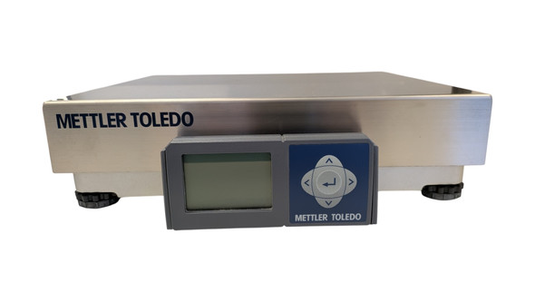 A front-facing product shot of a Mettler Toledo BCA-222 industrial shipping scale against a solid white background. The scale features a brushed stainless steel top platter with "METTLER TOLEDO" printed in navy blue on the left front lip. A dark gray digital display unit is mounted at the center front, featuring a blank LCD screen on the left and a blue control pad with cross-pattern arrow navigation keys and a center enter symbol on the right. Four adjustable black leveling feet are visible beneath the cast-metal base.