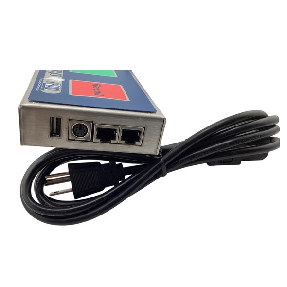 Close-up profile view of the left-hand interface panel of the stainless steel iPadSX bump bar unit, showcasing a standard USB port, a legacy round mini-DIN keyboard port, and two matching RJ11/RJ45 serial COM communication ports, with a coiled black power cable underneath.