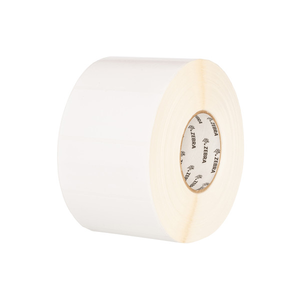 A three-quarter view of a roll of white thermal labels set against a plain white background. The labels are wound onto a cardboard core that features the Zebra logo printed repeatedly in black on the inside. The roll shows the smooth, bright white surface of the labels on the front and the tightly layered, light-tan edges of the label backing on the side.