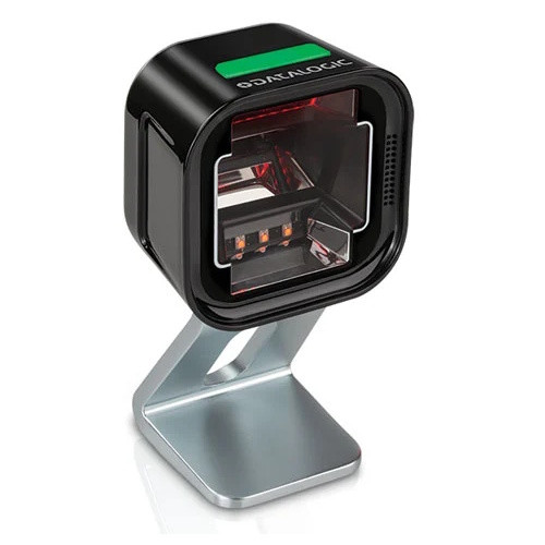 A studio product shot on a clean white background showcasing the black Datalogic Magellan 1500i presentation barcode scanner. The scanner features a compact, cube-like design with rounded corners and a glossy black finish, casting a soft reflection below. It is mounted onto an elegant, angled metallic silver desktop riser stand. The large front window displays the recessed 2D omnidirectional imaging optics framed by a thin red interior light border, while the top of the scanner features a prominent bright green decorative indicator strip next to a white stamped "DATALOGIC" logo.