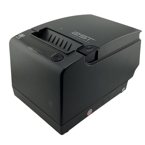 An angled front view showing the top and left side of the matte black printer. The "2ST TECHNOLOGY" logo is prominent on the top cover near the slotted paper exit. A circular paper feed button with an upward arrow and the small NCR circular logo are at the front left corner. The device has a rounded front edge, and a small regulatory label is visible on the bottom edge near the rear.