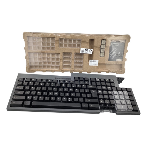 Straight-on front view of an iron gray Toshiba POS keyboard featuring a standard QWERTY layout and clear keycap covers on the right-side numeric keypad, set in front of its cardboard packaging tray.