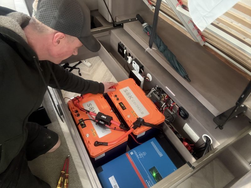 RV Solutions technician installing twin SOK lithium batteries and a Victron MultiPlus-II inverter in a motorhome
