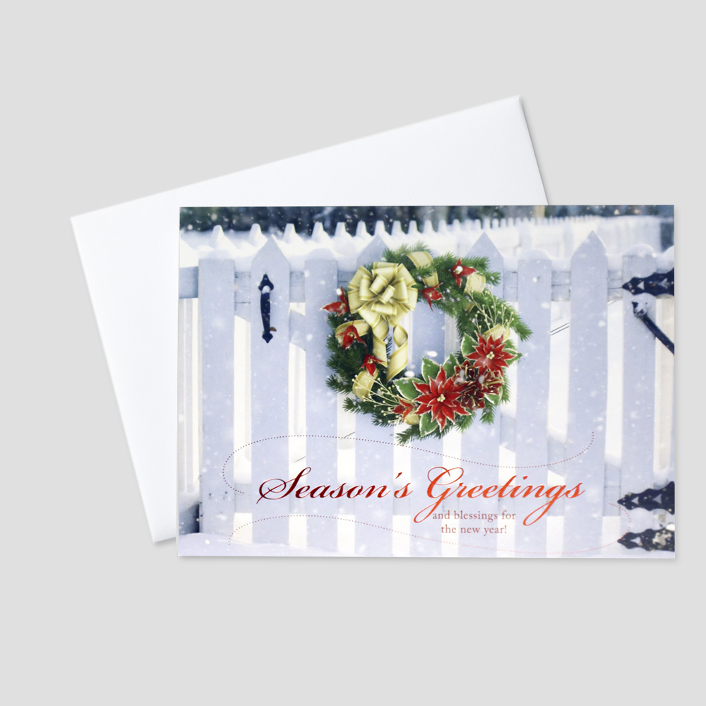 Professional Holiday greeting card with a holiday wreath on a white picket fence and a Season's Greetings message in red foil print