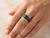 Close-up of a model’s hand wearing a wide black and white diamond pavé ring in elegant, natural indoor lighting.