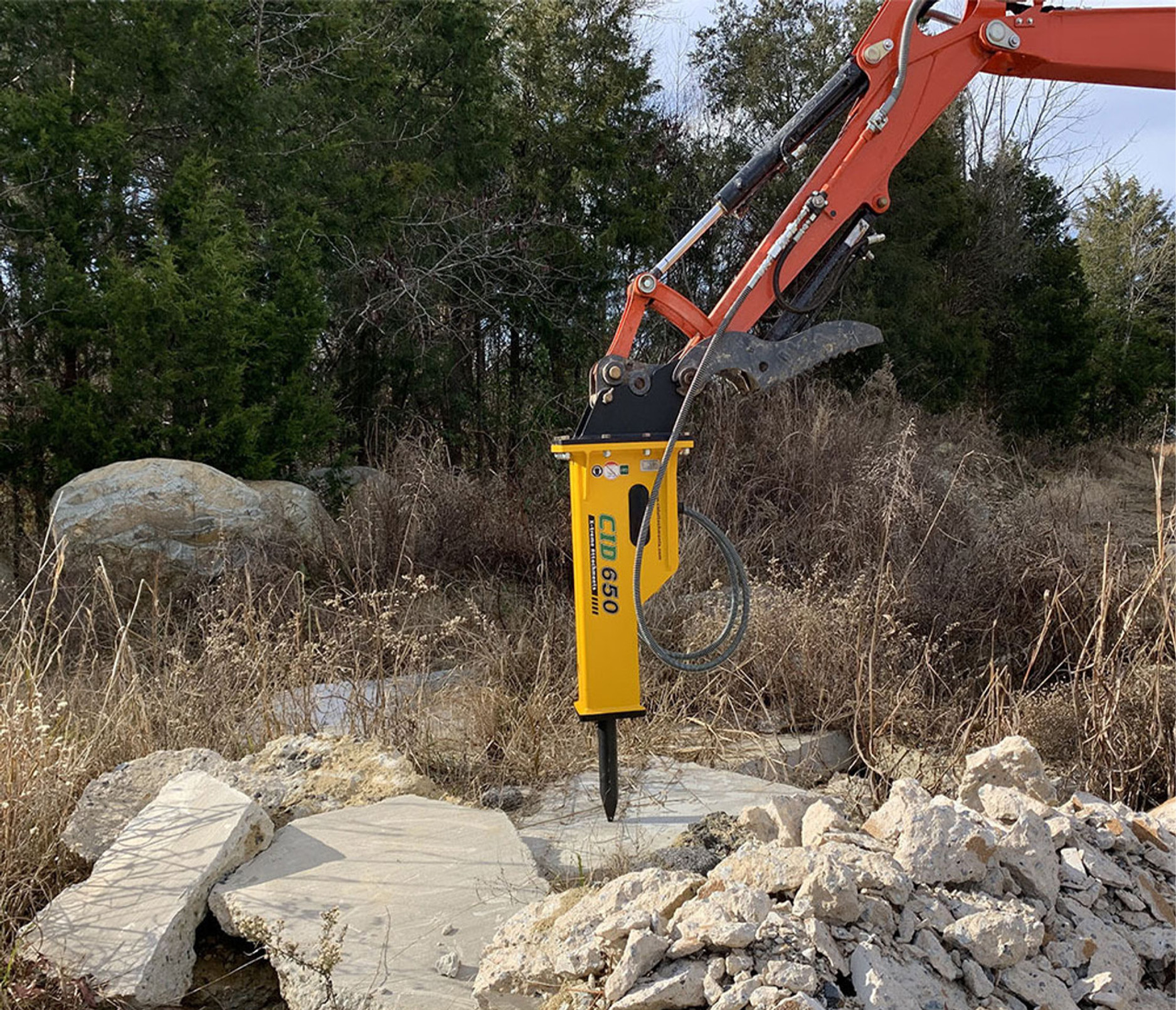 distant view of a cid excavator hydraulic concrete breaker attachment position over some rock 