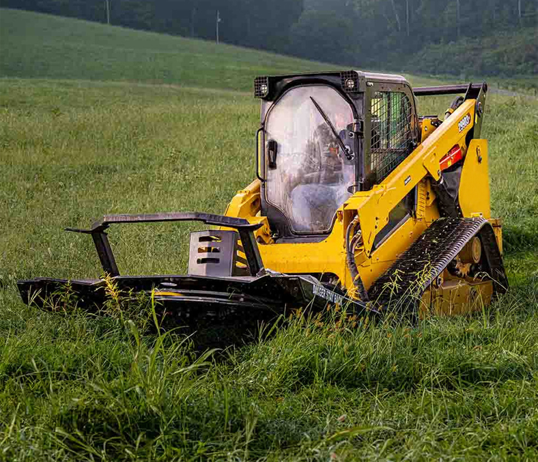 front angled view of a skid steer parked on grass with a cid heavy duty brush cutter attachment on the front 