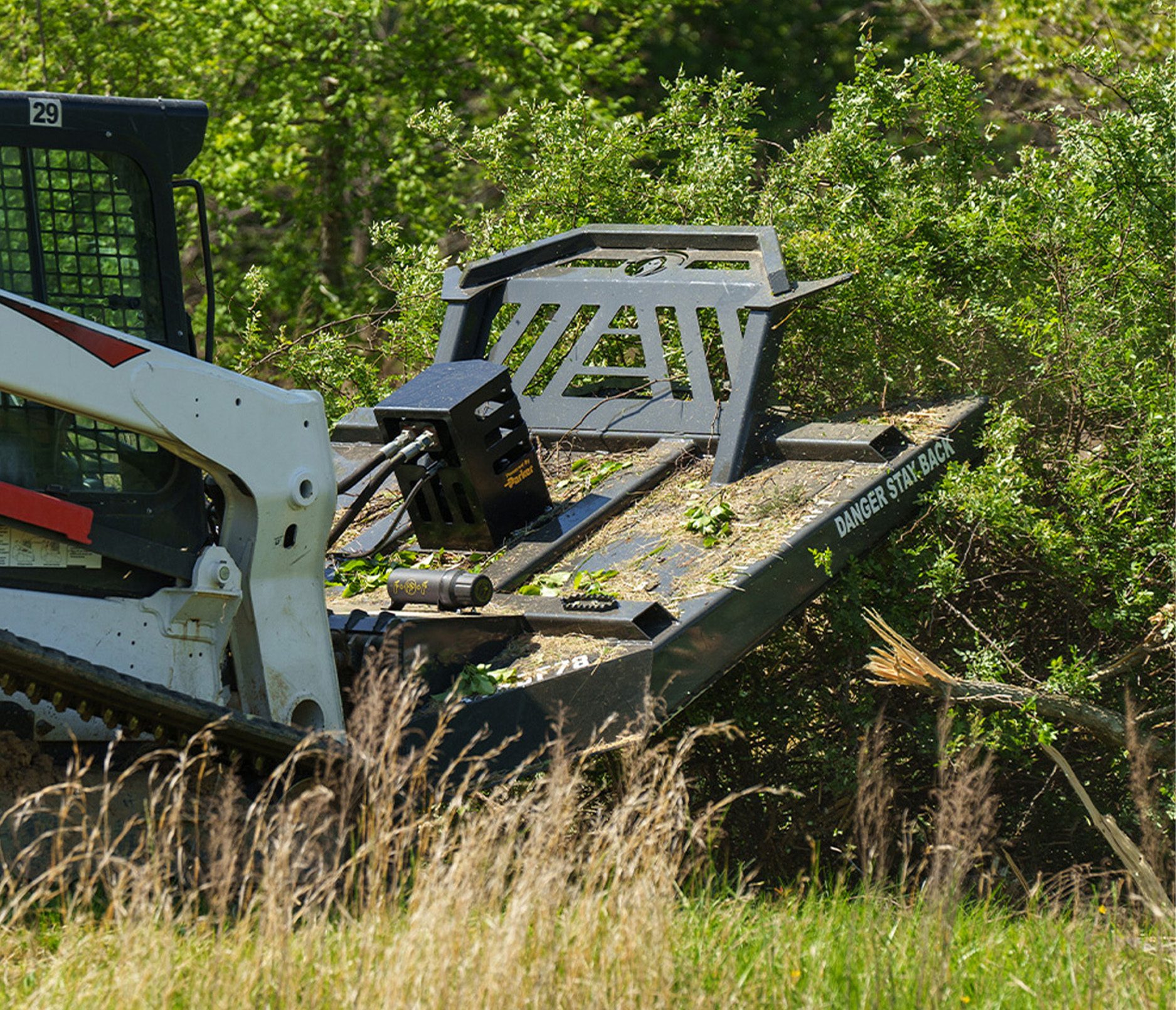 back angle view of a skid steer in thick vegetation with the CID Tree Reaper Brush Cutter Attachment on the front