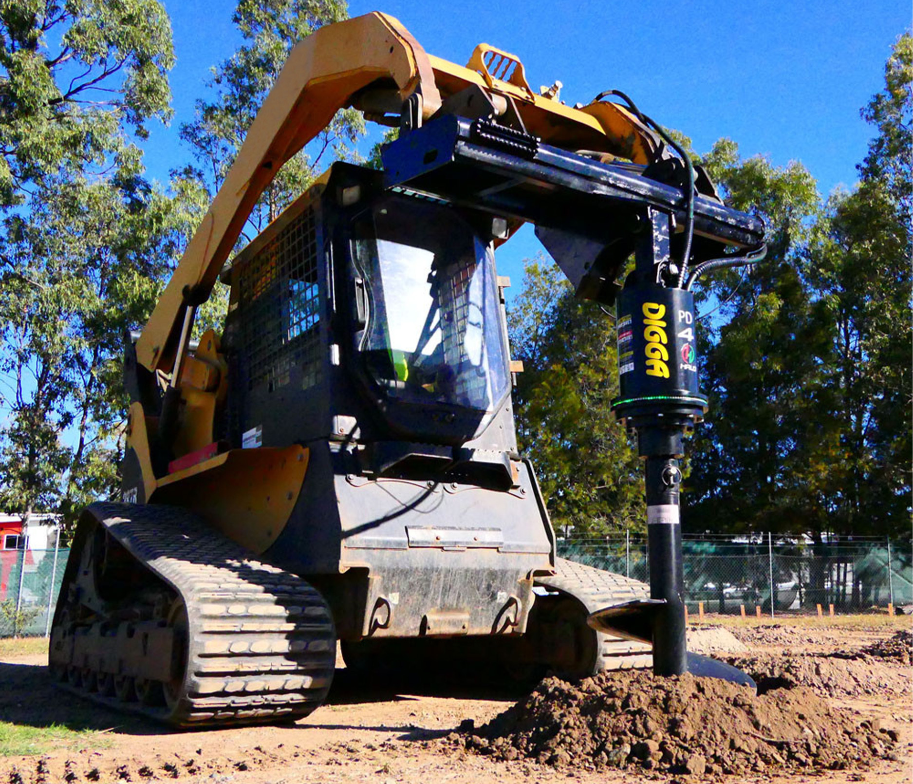 left-angled view of a skid steer parked on dirt with a digga heavy duty auger drive on the front, positioned to begin drilling