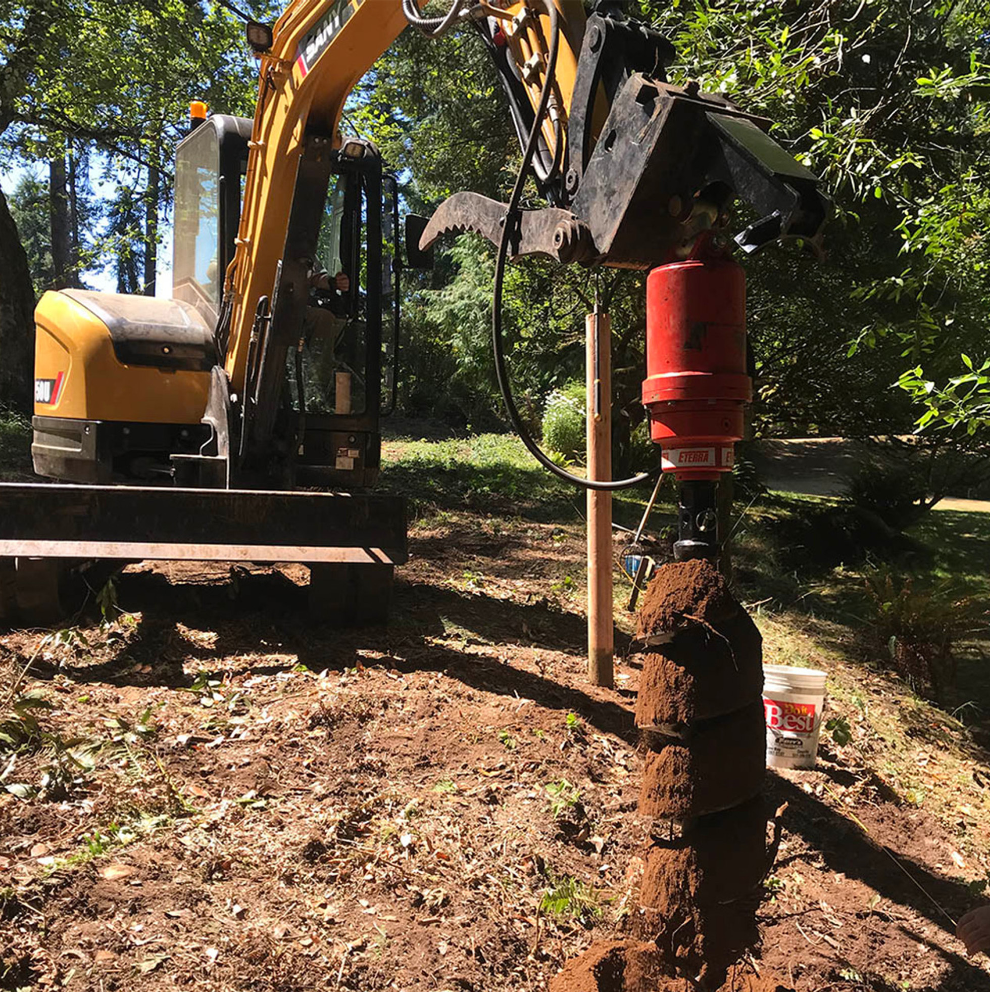 left angled view of an excavator parked on dirt with an eterra excavator auger attachment mounted on the boom