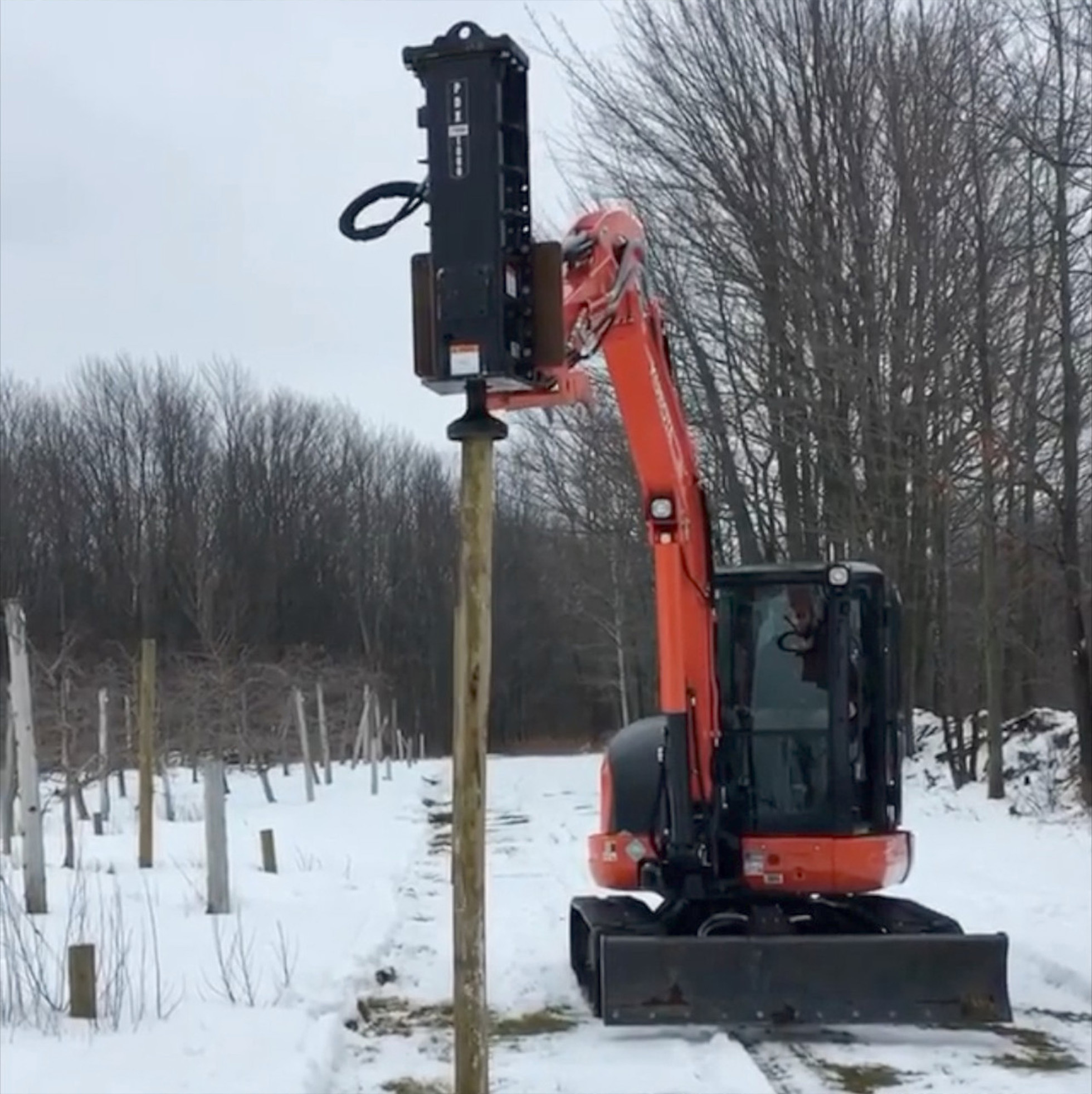 front view of an excavator with an eterra pdx-1000 post driver attachment on the boom pounding a post 