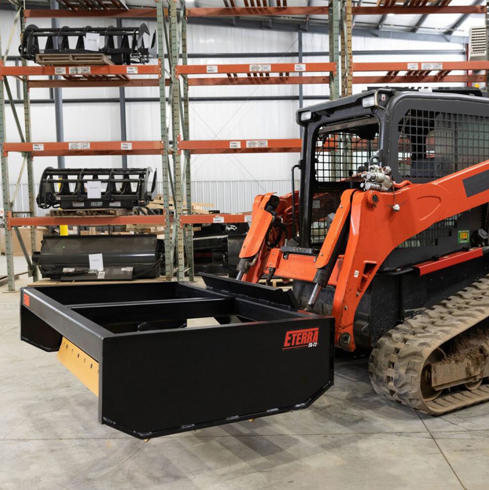 right-angled view of a skid steer parked in a warehouse with an Eterra Box Grader Attachment on the front