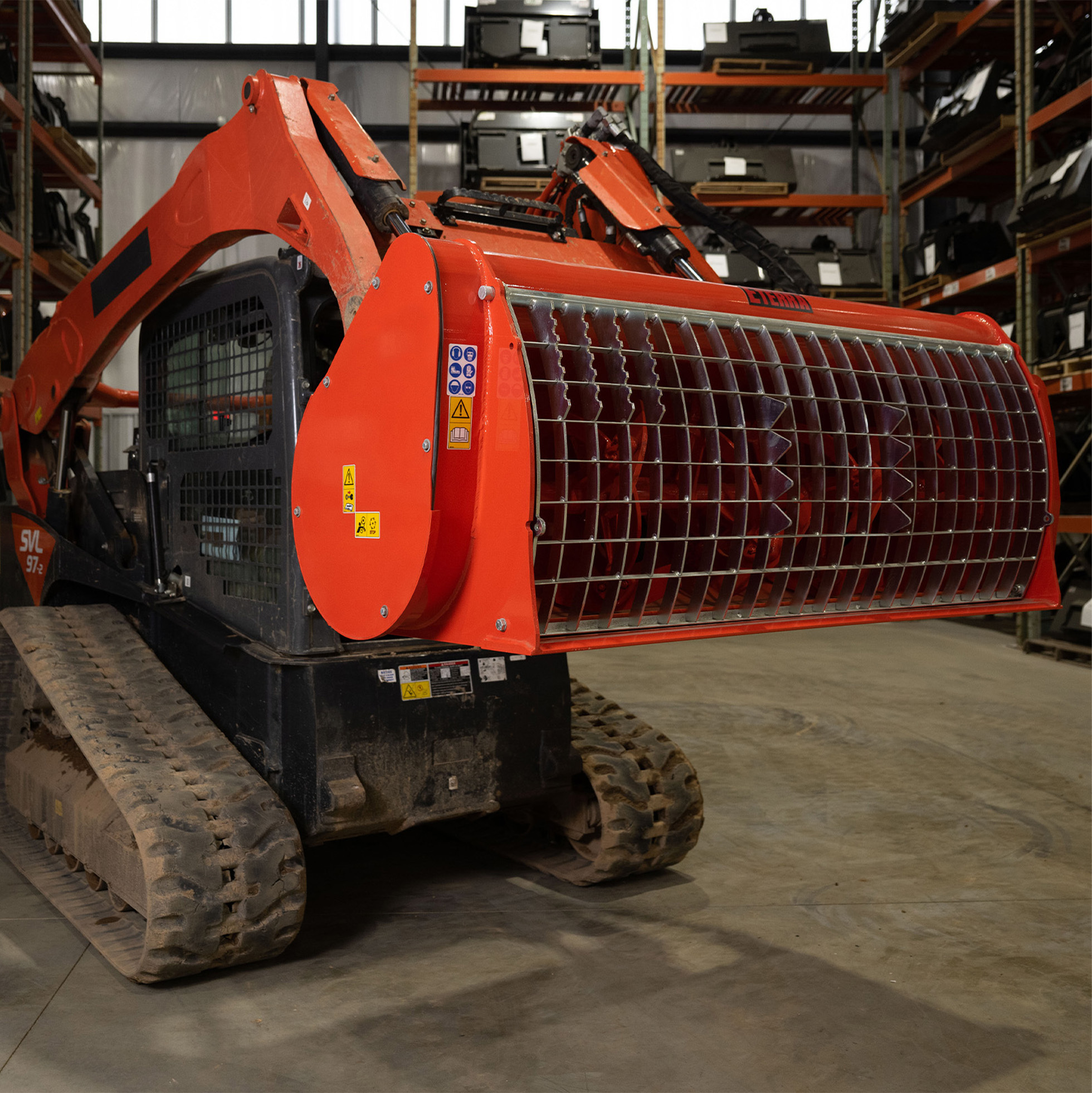 left-angled view of a skid steer parked a in warehouse with an eterra mix and go concrete mixer attachment on the front lifted, tilted up