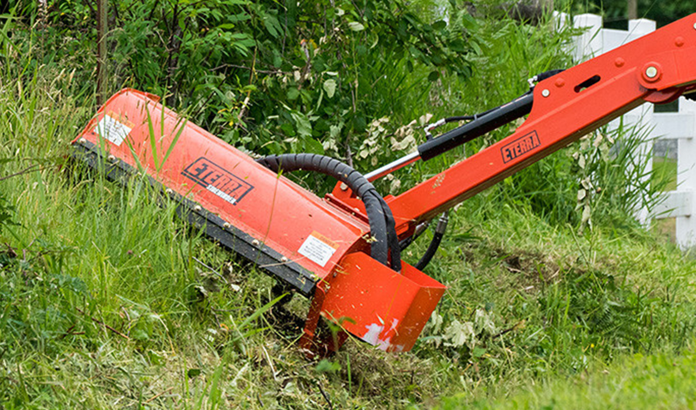 Skid Steer Flail Mower Attachment closeup action shot of the Eterra skid steer Sidewinder Flail Mower Attachment cutting grass on a boom-arm
