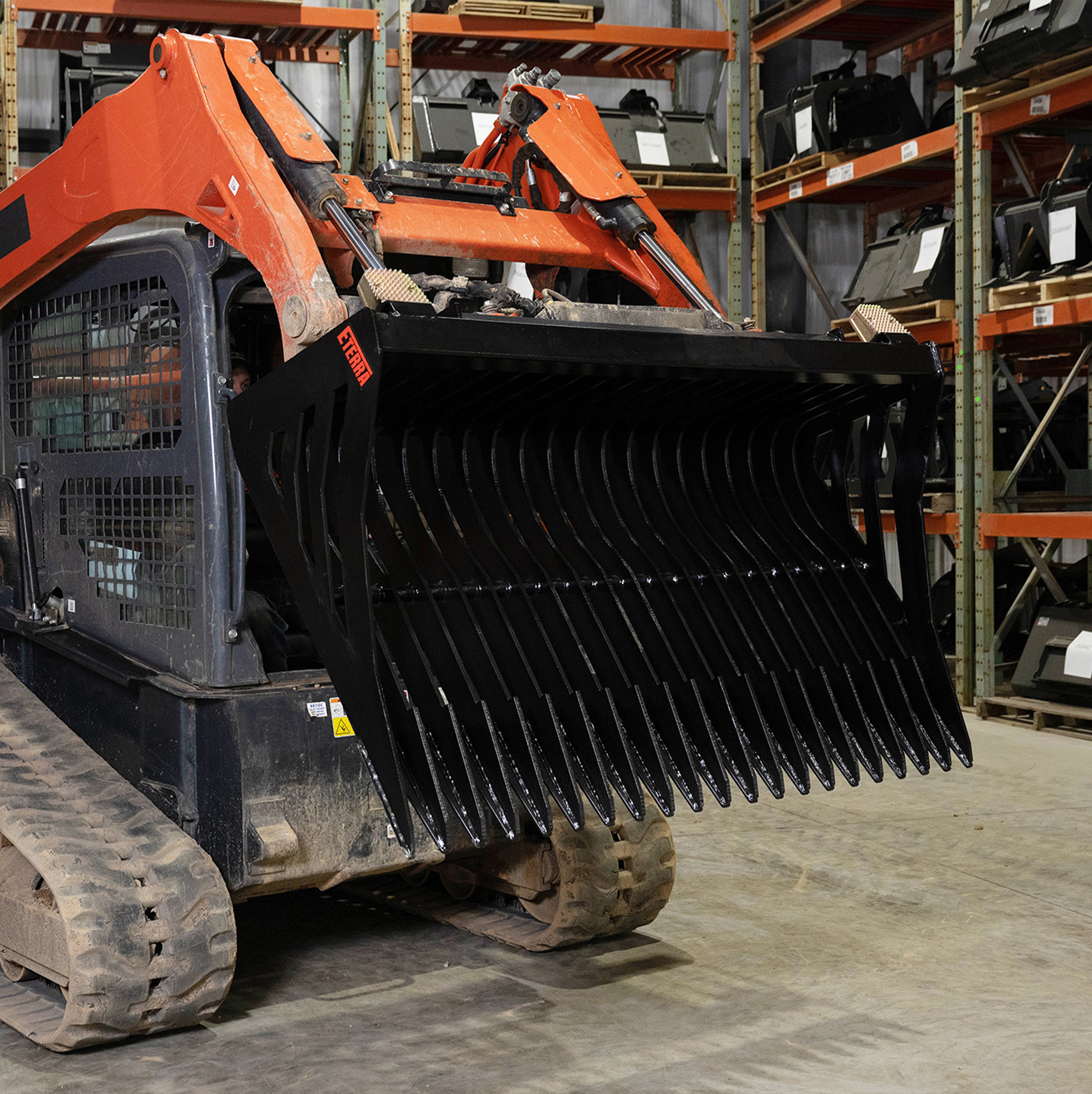 left-angled view of a skid steer parked a in warehouse with an eterra mix skeleton bucket attachment on the front lifted, tilted down