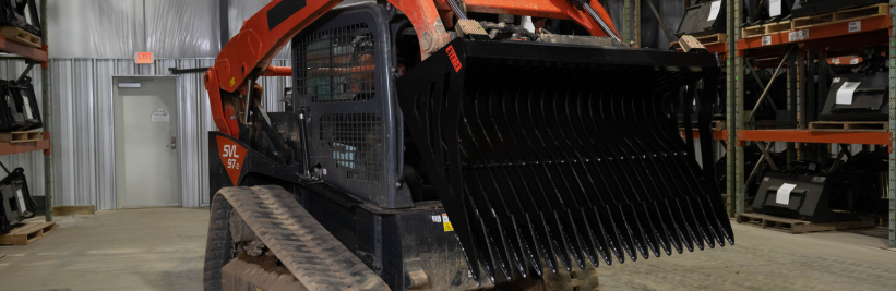 left angled view of a skid steer parked in a warehouse with an eterra skeleton bucket attachment on the front, lifted and tilted down