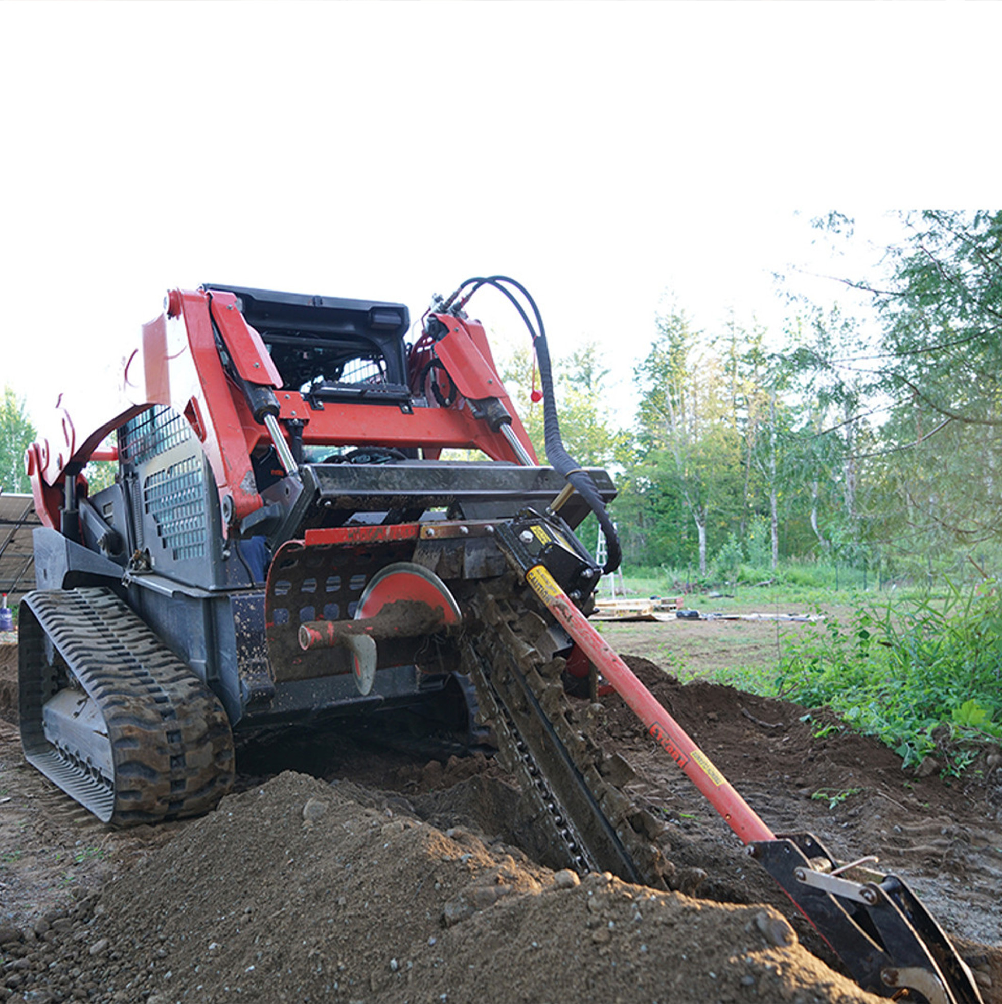 front left angled view of skid steer parked on a mound of dirt with an eterra 4 foot trencher attachment on the front