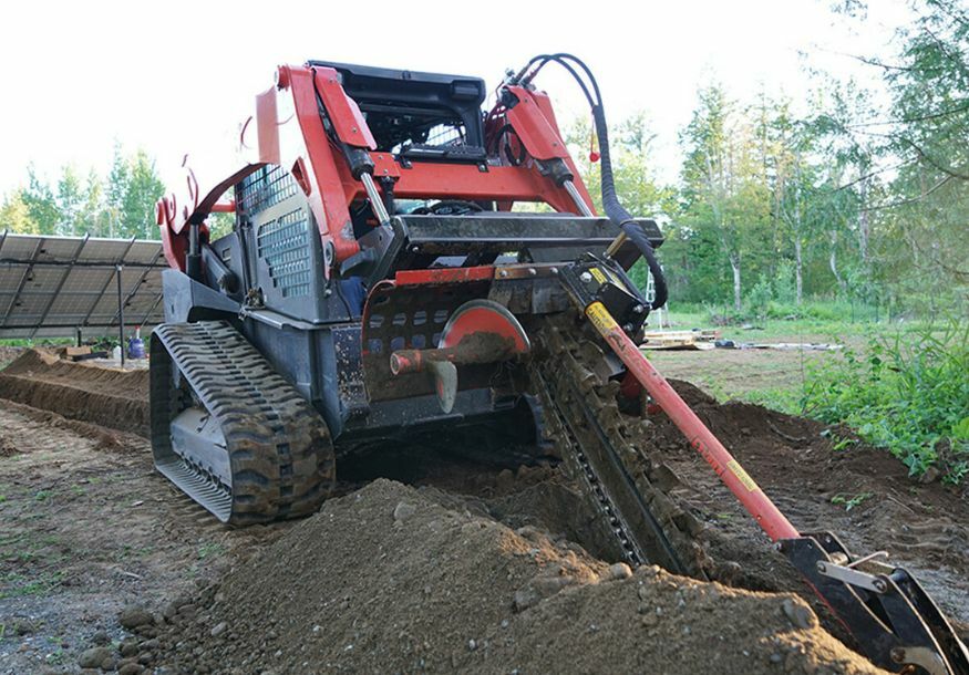 front left angled view of skid steer parked on a mound of dirt with an eterra 4 foot trencher attachment on the front 