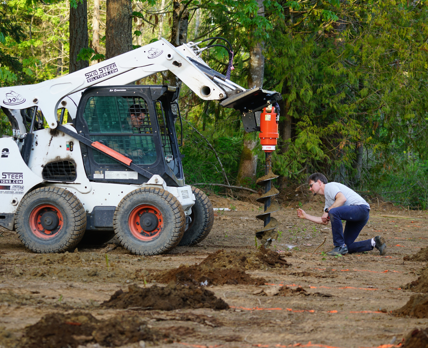 left side angle of a skid steer parked on dirt with an eterra auger attachment on the front