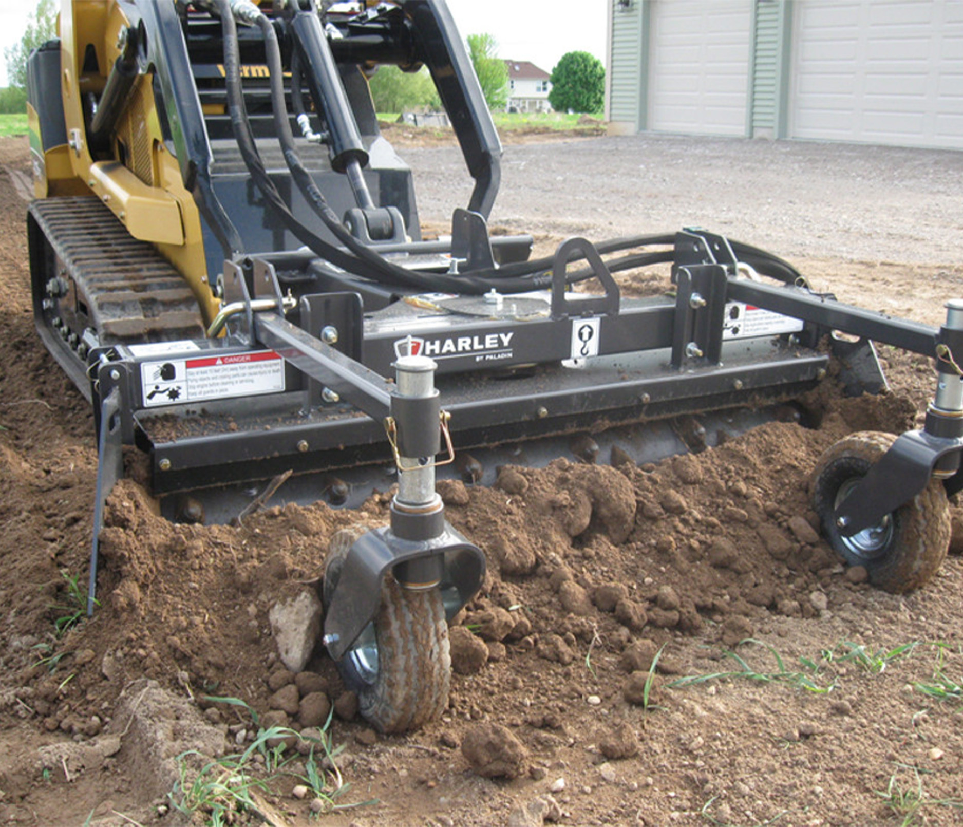 front angled view of a mini skid steer parked on dirt with a harley rake attachment on the front