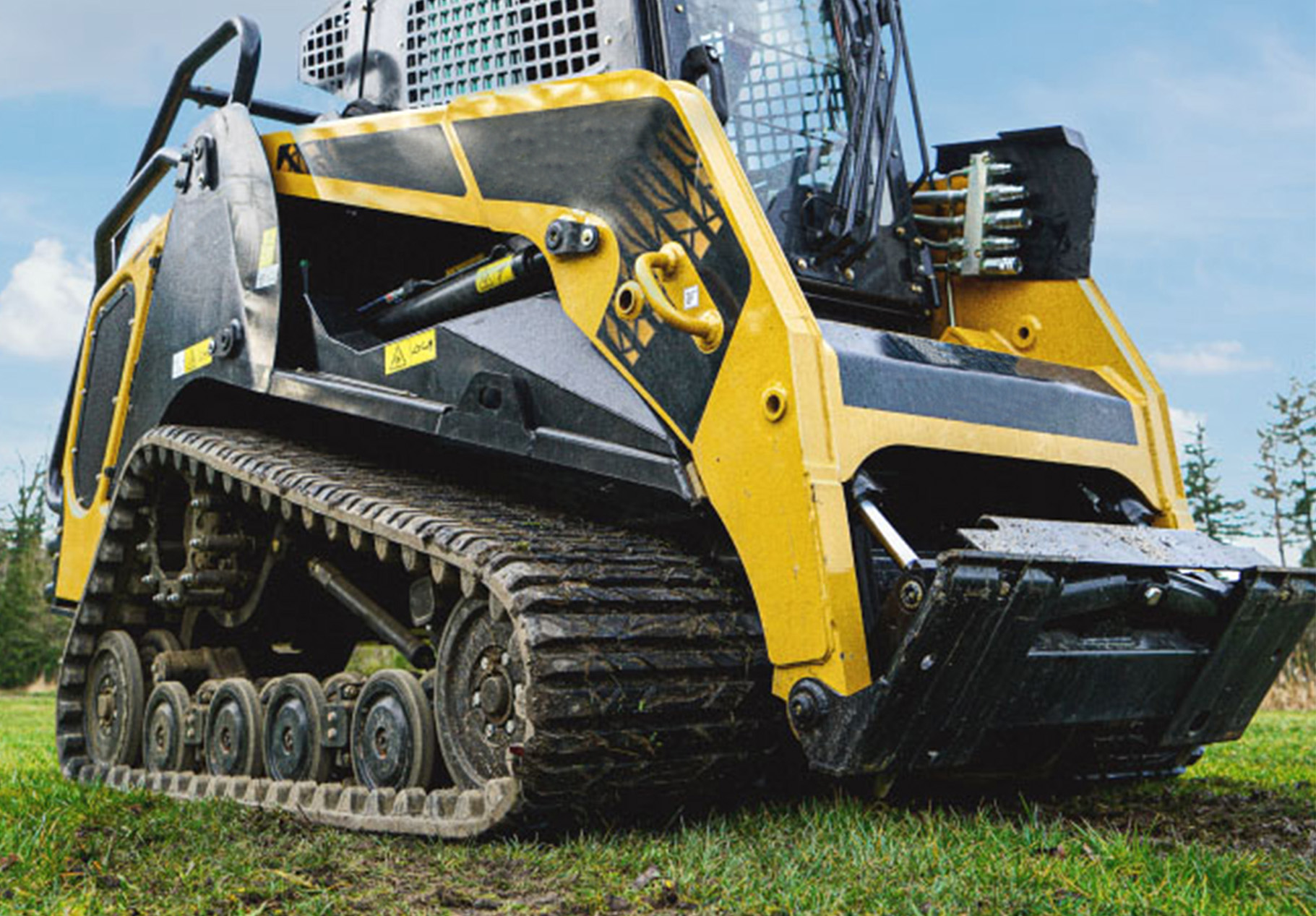 left angled view of a skid steer parked on grass showcasing muddy ctl tracks