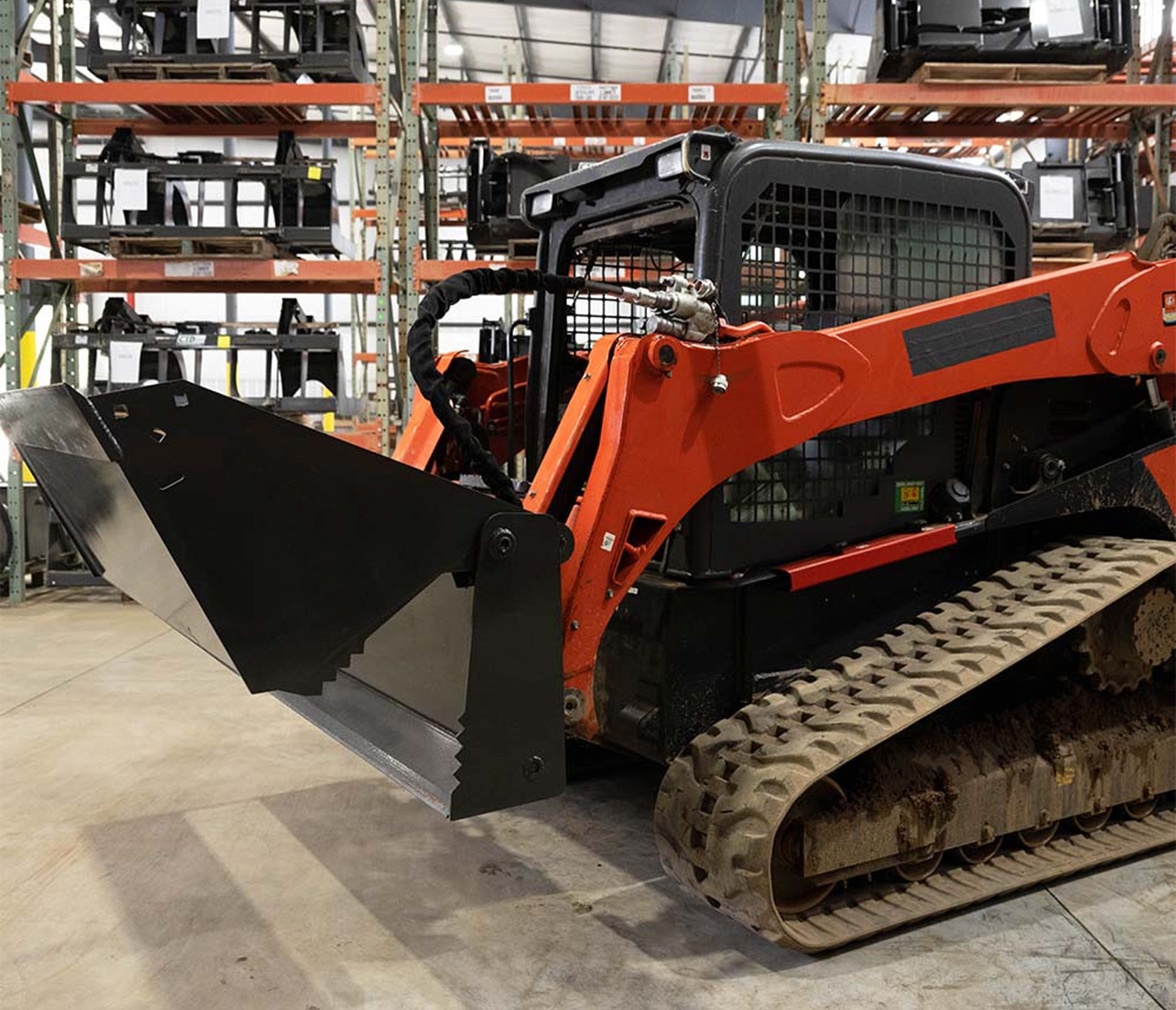 side angled view of a skid steer parked in a warehouse with a skid steer basics 4-in-1 bucket on the front