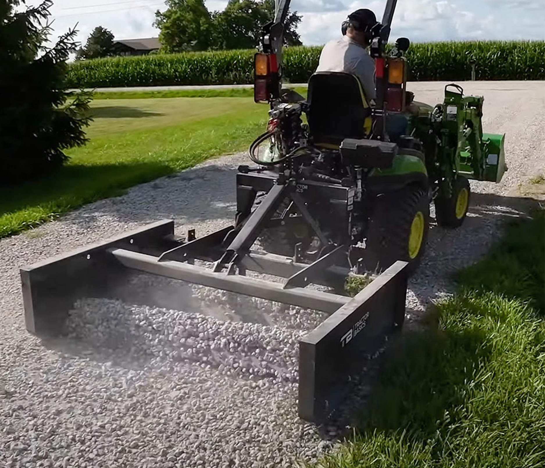 right angled view of the tractor basics dual edge grader attachment hitched to a tractor grading a gravel driveway