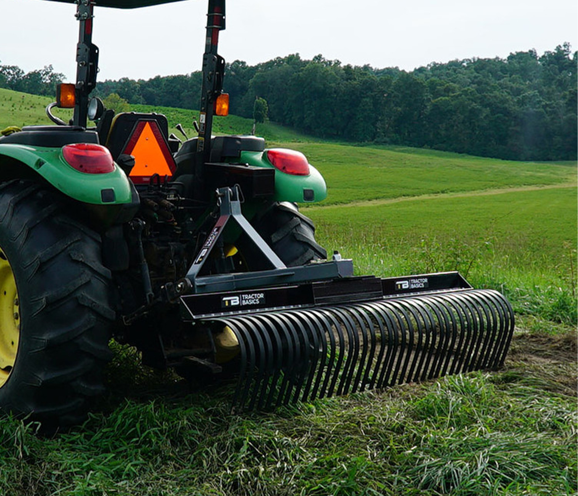 left angled view of a tractor parked in a field with a tractor basics landscape rake attachment on the front