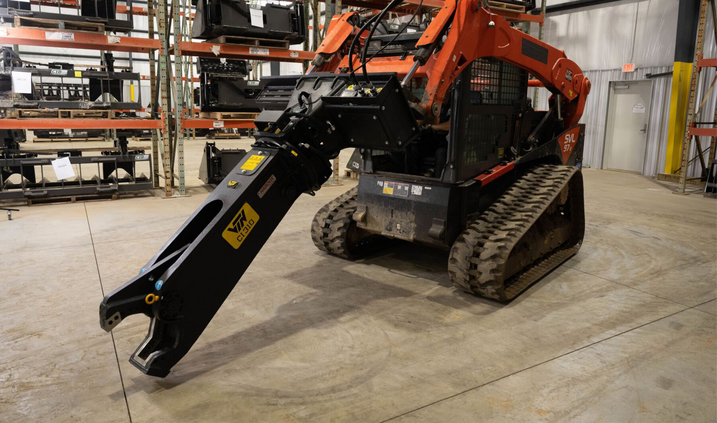 Side angled view of a skid steer parked in a warehouse with a VTN Scrap Shear Attachment on the front, open