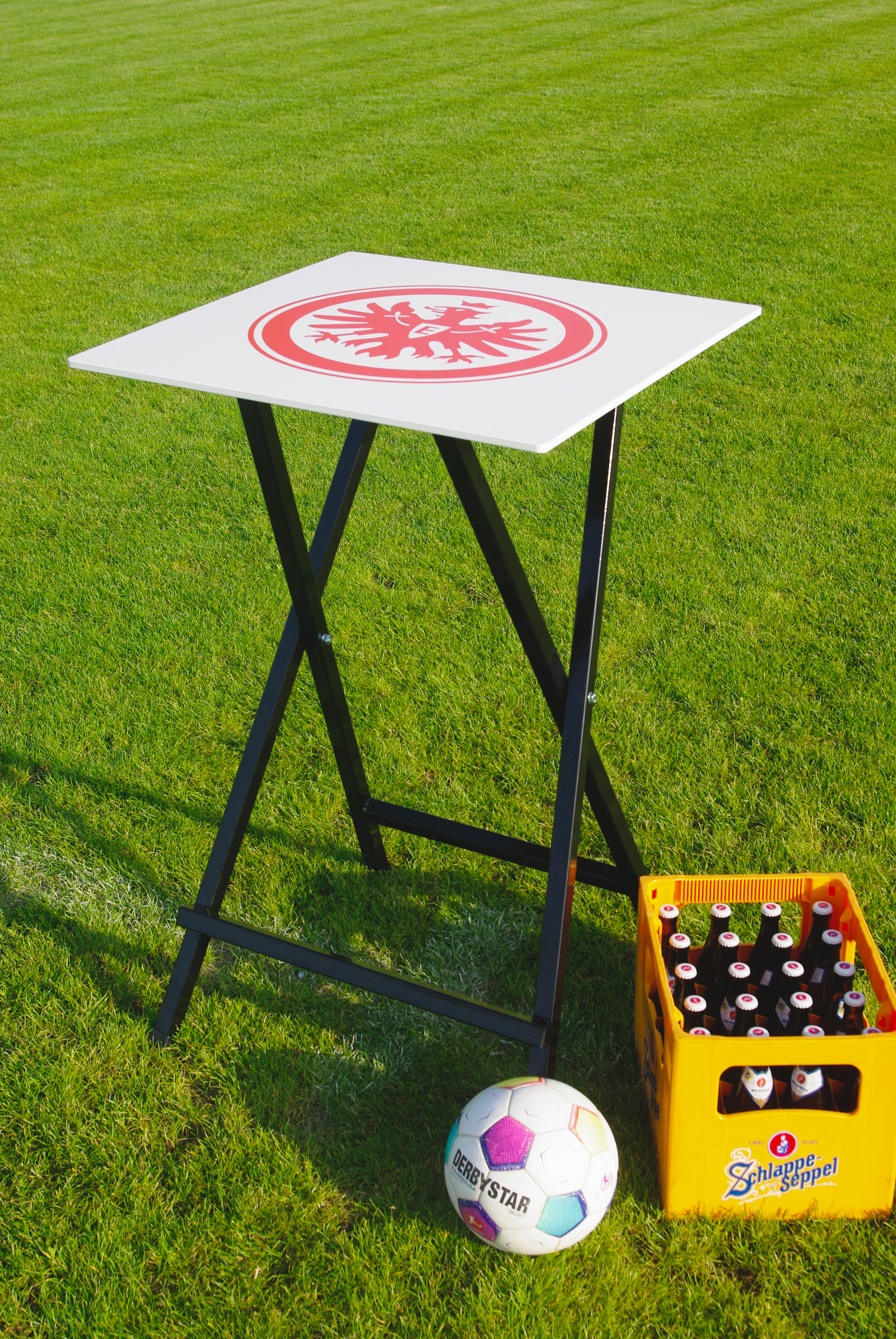 Stehtisch mit Eintracht Frankfurt Logo neben Fußball und Bierkasten auf Rasen
