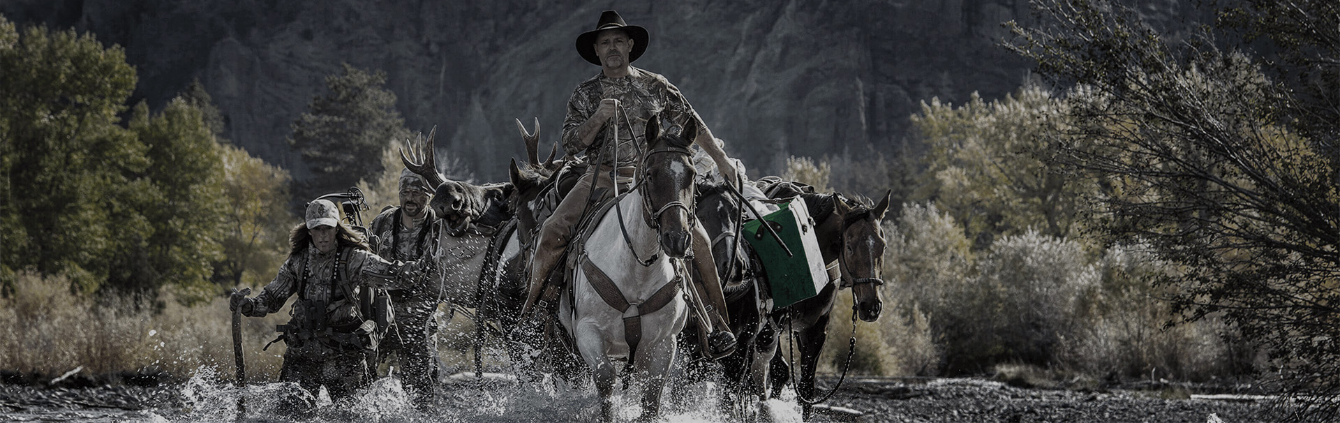hunters riding horses across a river