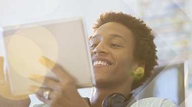 Person smiling while using a tablet, with headphones around their neck.