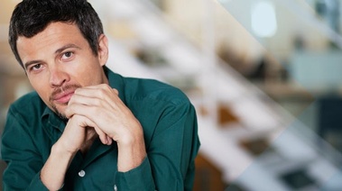 A man dressed in a green shirt looks into the camera, presenting a composed and attentive appearance.