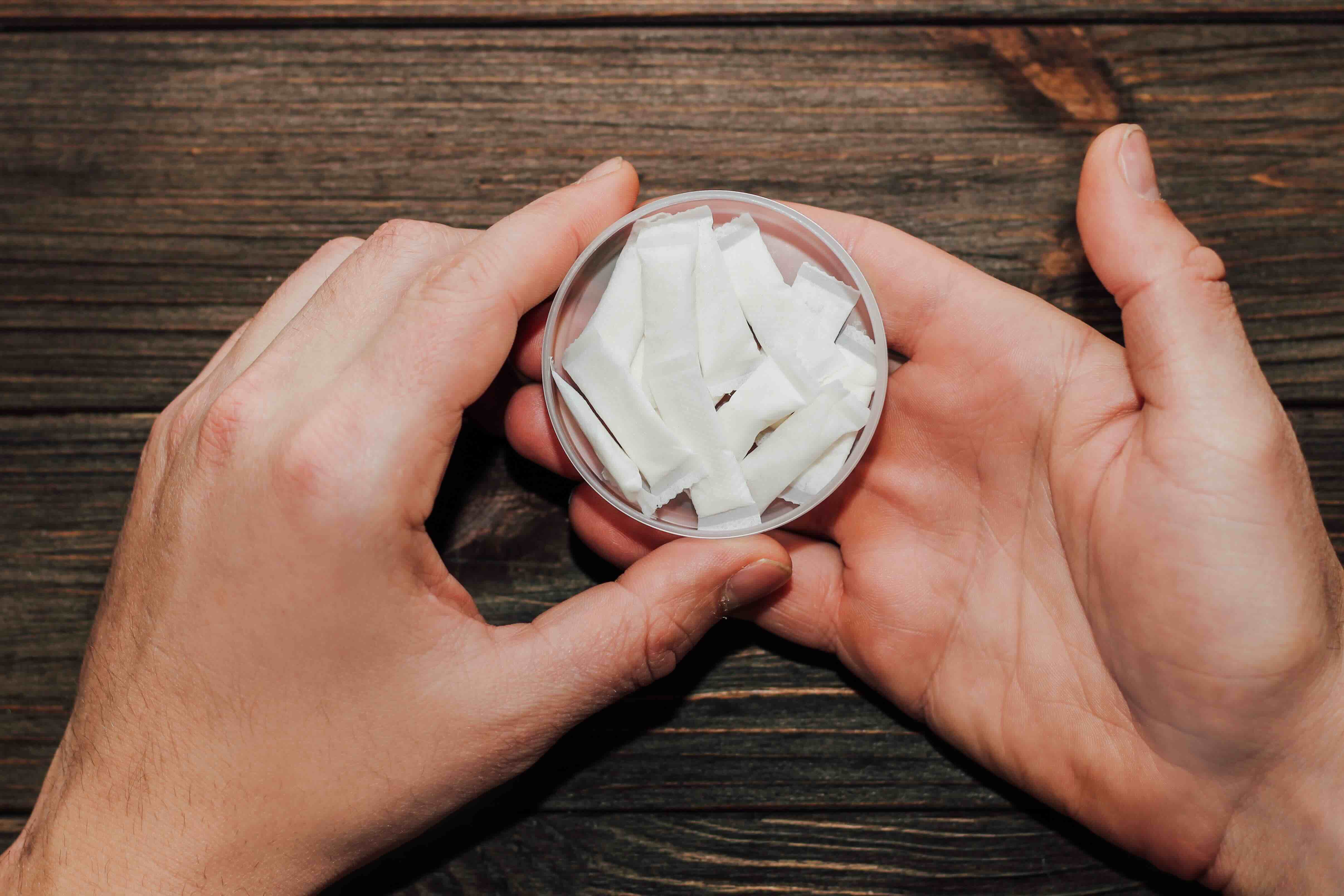 a pair of hands holding a tin of white nicotine pouches