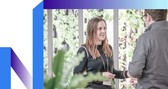 Two individuals engaged in conversation, standing in front of a lush green plant wall,