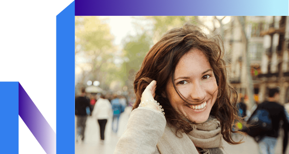 A smiling woman with wavy brown hair stands on a busy street, wearing a scarf.