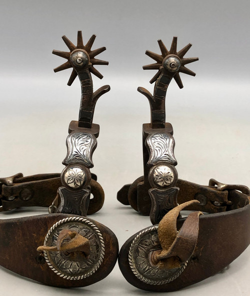 California style spurs, silver mountings, leather straps, single mounted spurs, engraved silver, inlaid silver strips, 10 point rowel,  Circa early 1900s