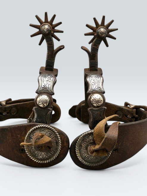 California style spurs, silver mountings, leather straps, single mounted spurs, engraved silver, inlaid silver strips, 10 point rowel,  Circa early 1900s