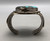 larger central turquoise stone, hand stamped designs, filework, twisted wire, silver dots, and silver applique