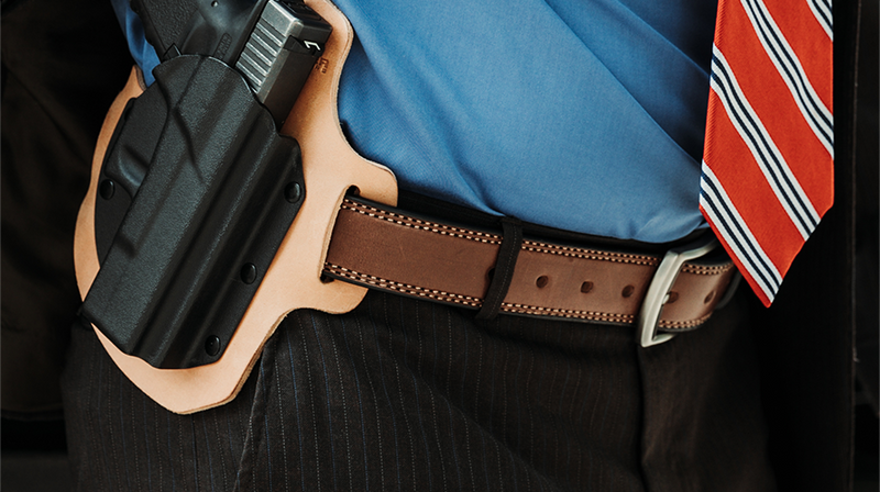 Man showing leather belt with holstered firearm attached.
