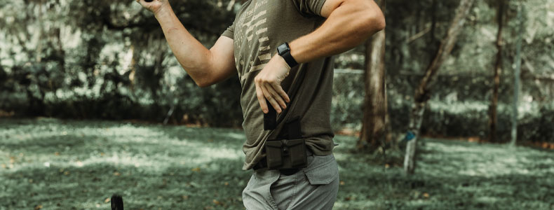 Outdoors photography of a guy drawing a gun magazine from his Magdraw Double OWB Holster to reload his handgun.