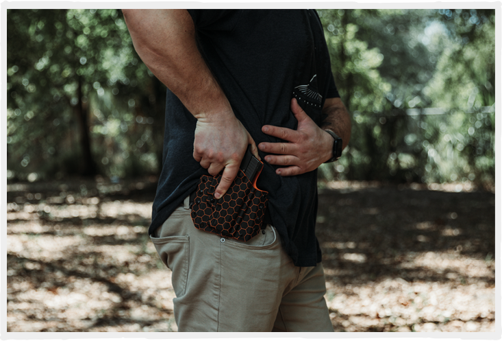 Man in a wooded area preparing to draw a firearm from a orange hexagon pattern LightDraw holster.