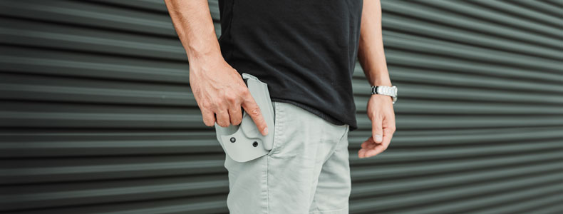 A guy placing his Pocket Locker Holster with his attached handgun on his right side front pocket on his shorts. 