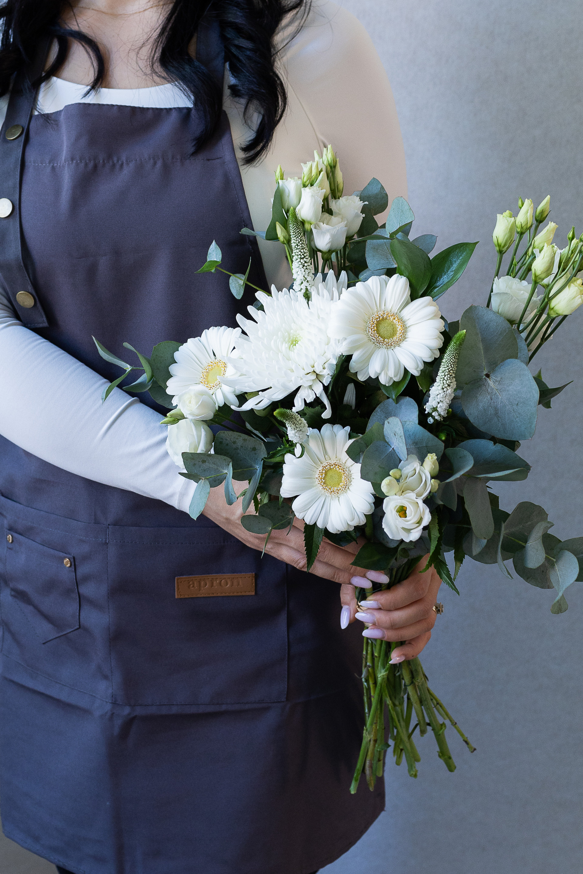 Florist holding a bouquet of white gerbera, chrysanthemum, lisianthus, veronica, and eucalyptus foliage.