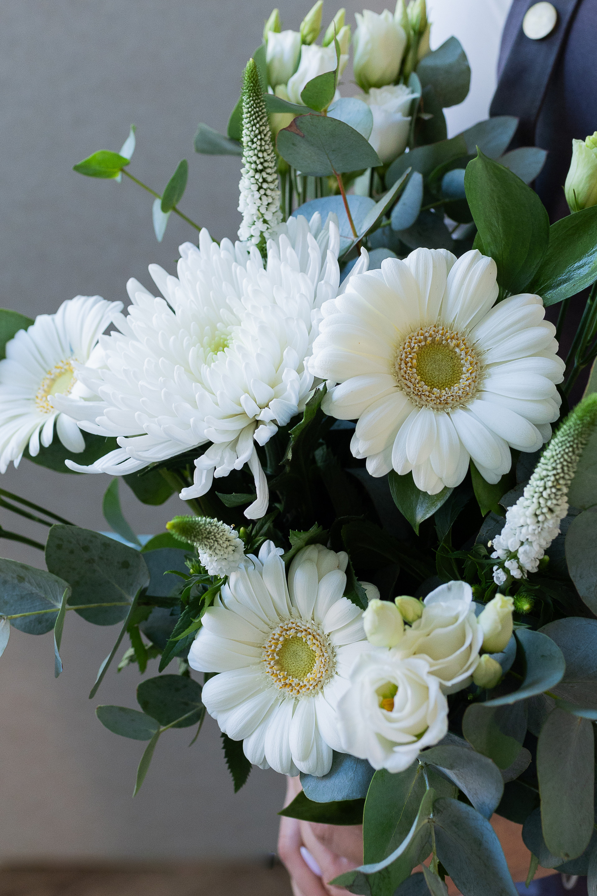 Close-up of a white floral bouquet with gerbera daisies, chrysanthemum, lisianthus, veronica, and eucalyptus foliage.